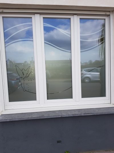 Fenêtre à trois vantaux d'une façade enduite claire dont le vitrage porte un film à effet sablé ajouré d'une fée à baguette, d'étoiles et de vagues