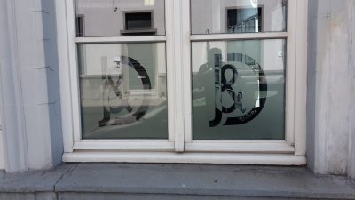 Fenêtre à deux vantaux d'une façade grise dont les vitrages inférieurs portent un film à effet sablé ajouré d'un monogramme entrelacé
