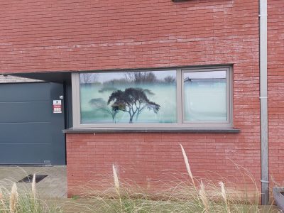 Fenêtre en bandeau d'une façade en briques rouges dont le vitrage porte un film imprimé translucide d'arbres dans la brume