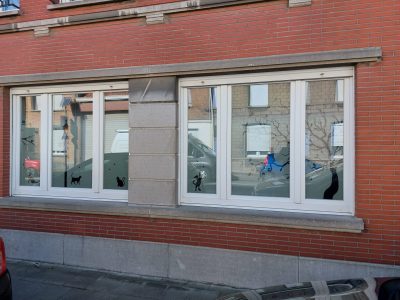 Deux fenêtres d'une façade en briques rouges dont le bas du vitrage porte un bandeau de film à effet sablé orné de silhouettes de chats et de branchages