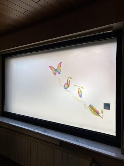 Fenêtre à châssis noir dont le vitrage porte un film à effet sablé plein rehaussé de papillons et de plumes imprimés en couleurs
