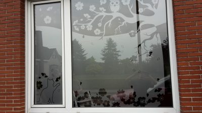 Fenêtre à châssis blanc d'une façade en briques rouges avec un film à effet sablé à motif de branche de cerisier en fleurs, avec un hibou perché et un chat assis
