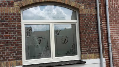 Fenêtre à imposte cintrée d'une façade en briques rouges avec un film à effet sablé personnalisé d'initiales calligraphiées, d'étoiles filantes aux angles et d'une phrase de bienvenue sur l'imposte