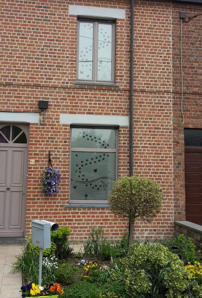 Deux fenêtres superposées d'une façade en briques rouges dont les vitrages portent un film à effet sablé à motif de chats, d'empreintes de pattes et de papillons