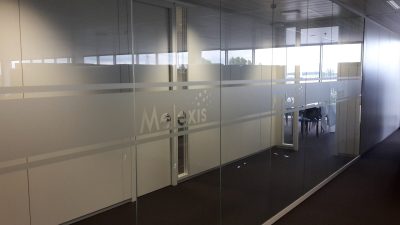 Cloison vitrée d'une salle de réunion avec deux bandes horizontales de film à effet sablé et, entre elles, un logo d'entreprise en film sablé répété sur chaque panneau